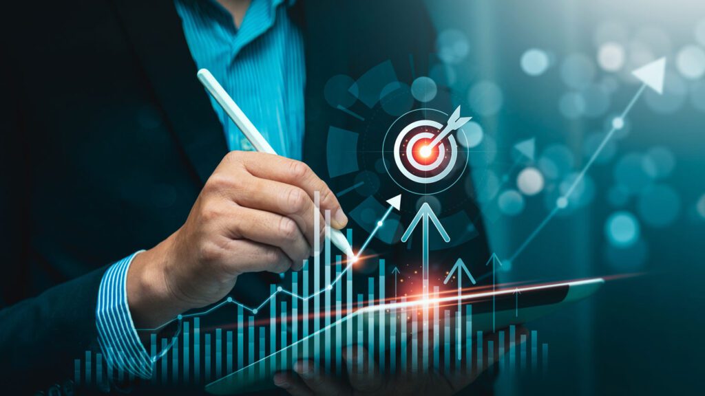 A person in a suit uses a stylus on a tablet with digital graphs, arrows, and a target icon symbolizing business growth and goal achievement.